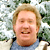 Static pixelated image of a person with light brown hair wearing a blue shirt against a blurred green and white background.