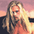 Pixelated static image of a person with long wavy hair against a sunset sky background, wearing an orange top and dark outer garment.