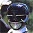 Pixelated static image of a dark helmeted figure with blue accents and white highlights against a muted green background.