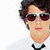 Pixelated image of a person with dark curly hair, red-tinted sunglasses, white shirt, and black bow tie against plain background.