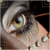 A close-up of a human eye with long eyelashes, brown and white beads on the cheek, and gold geometric patterns in the background.