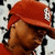 A person wearing a red cap with a white logo and red shirt, shown in three sequential poses against a black-and-white patterned background.