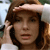 A pixelated close-up of a person with brown hair wearing a light-colored headband, hand raised near the head, against a blurred background with light and dark tones.