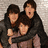 Three people in dark and light clothing pose closely together with arms around each other against a textured background, with green text elements surrounding the image.