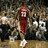 A basketball player in a red uniform with number 33 stands on a court, facing away from the viewer toward a blurred crowd.