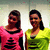 Two people stand side-by-side in a pixelated image; one wears a pink top with black text, the other a yellow-green top with black text, against a light background.
