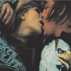 Two people kiss closely; one wears a blue patterned sweater, the other a white shirt with an eagle graphic.