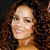 A pixelated close-up of a person with curly brown hair, light skin, and a smiling expression against a dark background.
