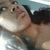 Pixelated image of a person with dark hair and light skin, wearing a white top against a blurred background.