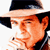 Static pixelated image of a man's face wearing a wide-brimmed hat with visible cigarette smoke, rendered in orange and black tones on white background.