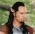 Static pixelated image of a person with long dark hair in a ponytail wearing a gray shirt against a green background.
