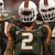 Pixelated image of football players in green jerseys with white number 2, orange accents, and white helmets featuring an orange stripe.