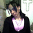 Pixelated image of a person with dark hair wearing a black jacket over a white top with purple accents, standing against a blurred background.