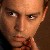Pixelated close-up of a person's face with light skin tone, dark eyebrows, and dark eyes, wearing a dark garment with a red patterned collar.