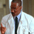 Static pixelated image of a person in formal attire with blurred background, likely from an older digital media source.