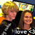 Two people stand side-by-side; the person on the right wears a white shirt while the left wears dark clothing with light patterns. A black banner with 'love <3' text appears below them.