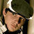 Pixelated close-up of a person wearing a dark green cap with a white brim, light skin tone, and dark hair visible beneath the cap.
