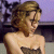 Pixelated static image of a woman with brown hair wearing a dark strapless top against a purple and gray background.