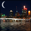 Night cityscape with illuminated buildings, a bridge, and a crescent moon over water, showing animation changes in building lights and bridge reflections.