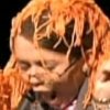 A close-up of a person with orange-blonde hair styled in thick, wet-looking strands, wearing a light-colored top with a visible collar.