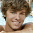 Pixelated image of a smiling person with brown hair on pink background, accompanied by red text and symbols.