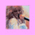 A pixelated image of a person with long brown hair holding a microphone, wearing a light blue and white outfit against a pink background.