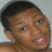 Pixelated close-up of a person with short dark hair, light brown skin, and a wide open mouth showing teeth, set against a light gray background.