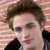 A pixelated close-up of a person with brown hair and light skin, wearing dark clothing against a brick wall background.