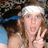 A pixelated static image shows a person with light brown hair wearing a white headband and blue strap, holding hands near their face against a blurred background.