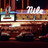 Pixelated image of a theater facade with columns and decorative elements, featuring a central marquee area and a dark background.