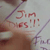 A hand holds a white object with red text, while another hand holds a white cylindrical object with a white cap.