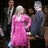 Pixelated image of a woman in pink dress with two men, overlaid with pixelated text on bright magenta background.