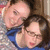 Two people in close physical proximity with one person's head resting on the other's shoulder, both wearing blue tops.