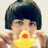 A person with short dark hair holds a yellow rubber duck with red beak near their mouth, hands positioned on either side of the duck.