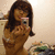 A person with long brown hair takes a mirror selfie with a silver digital camera, wearing a light-colored sleeveless top in a softly lit room with a blurred background.