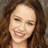 Pixelated close-up of a person with long brown hair, light skin, and a smiling expression showing teeth, set against a neutral background.