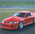 A red sports car with a white roof is positioned on a road, viewed from a low angle against a blurred green and blue background.