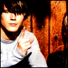 A person with dark hair and a light gray long-sleeve shirt points a finger toward the viewer against a wooden background.