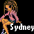 Pixel art of a female character with long brown hair, wearing a pink jacket over black top and blue shorts, standing against black background with partial text "Sydney" visible.