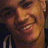 Pixelated close-up of a smiling person with light brown hair and visible teeth, wearing dark clothing against a blurred background.