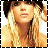 A pixelated image of a person with long blonde hair and dark bangs, wearing a light-colored top against a white background.