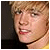 Static pixelated close-up of a person's face with light brown hair and visible facial features against a dark background.