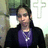 A pixelated static image shows a person with dark hair wearing glasses, a purple shirt, and black jacket against a blurred background with green and white elements.