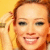A pixelated close-up of a person with light brown hair, smiling broadly against a yellow background.