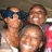 Two people in a close-up pose with one wearing dark blue headwear and the other smiling broadly, set against a blurred background.