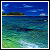 Pixelated landscape showing blue sky with light clouds, distant green and brown landmass, and layered water transitioning from deep blue to turquoise and green near the shore.