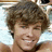 A pixelated image of a person with brown curly hair smiling, next to blue text reading "Mrs. Ryan Sheckler" on a light background.