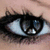 A close-up of a human eye with black eyeliner and mascara, showing subtle animation changes in the iris reflection.