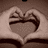 Two hands form heart shapes against a brown background, with subtle pixel-level variations between frames.