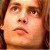 Pixelated close-up of a person's face with brown hair, brown eyes, and a neutral expression, rendered in warm tones.
